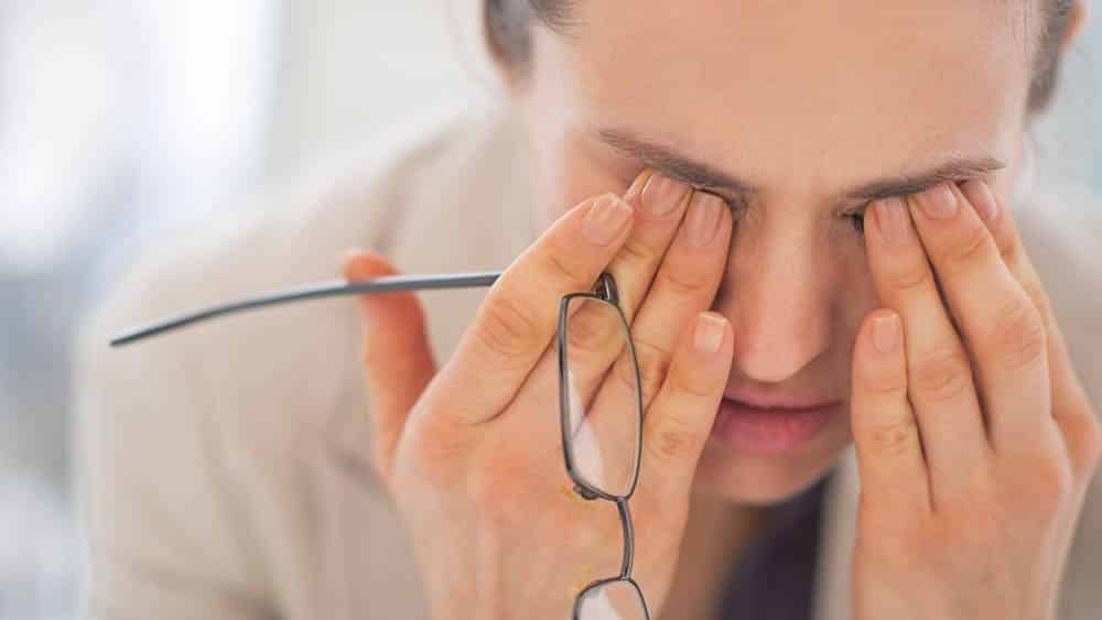 Mulher com roupa social esfregando os olhos demonstrando exaustão (síndrome de burnout).