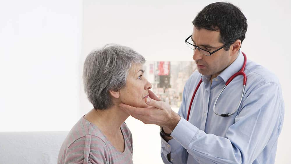 Médico apalpando gânglios do pescoço de uma mulher no consultório.