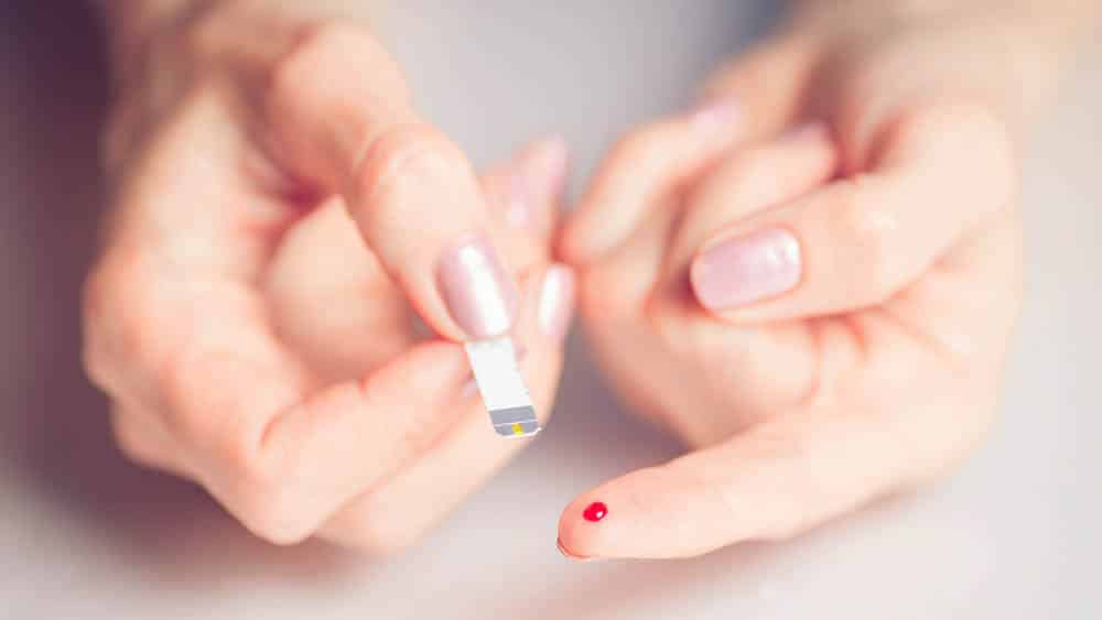 Close em dedo de mulher com gota de sangue e uma fita usada para medir glicemia, controle necessário para portadores de diabetes.