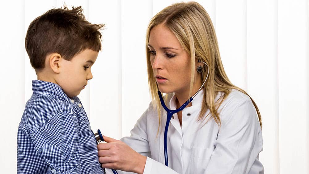 Médica auscultando o coração de um menino com um estetoscópio.