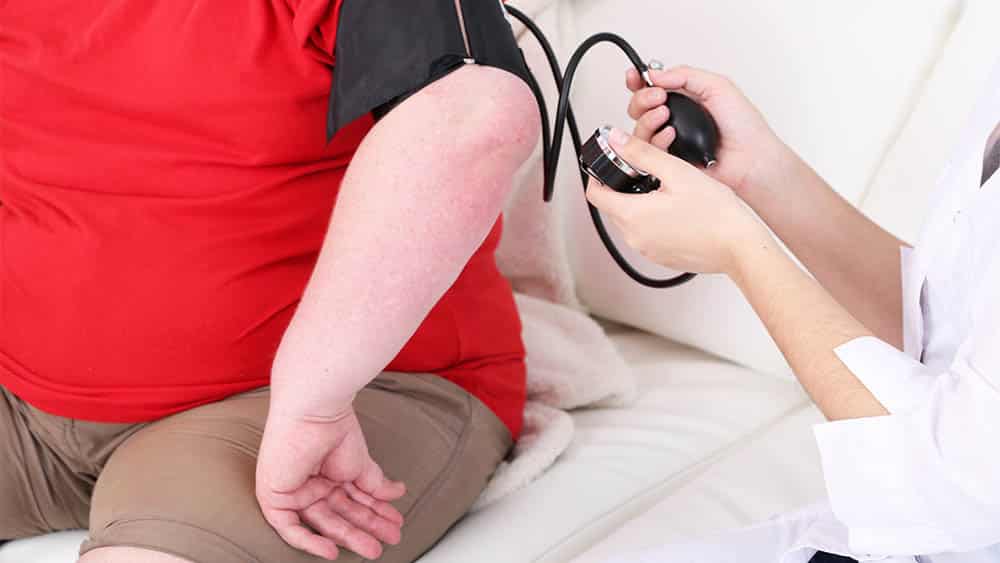 Médica medindo a pressão de uma pessoa obesa.