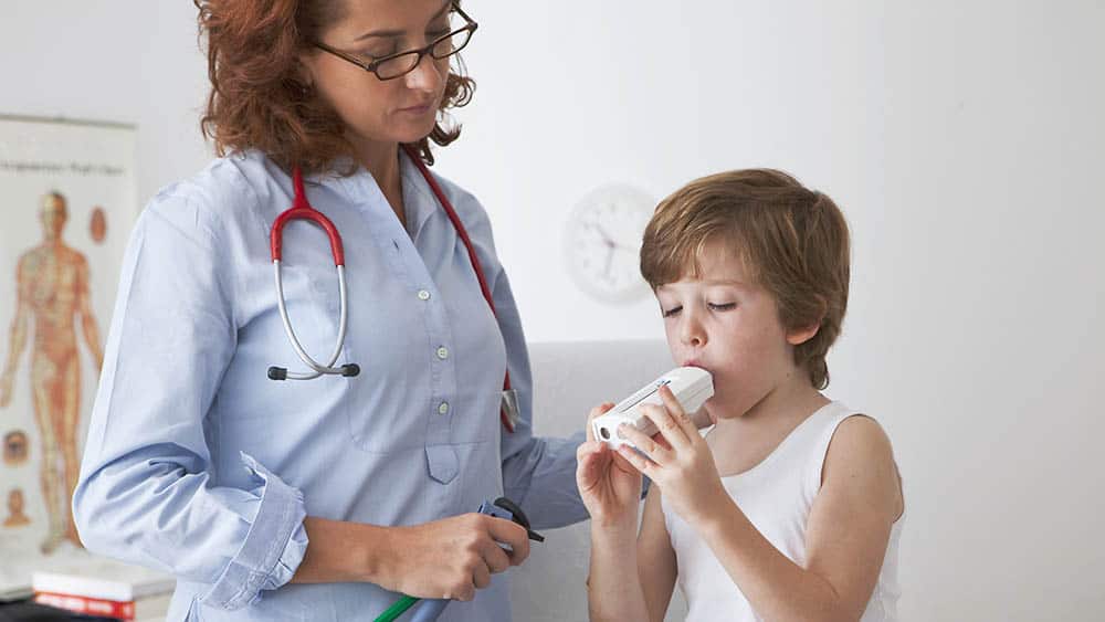 Menino soprando em aparelho de espirometria com médica ao lado.