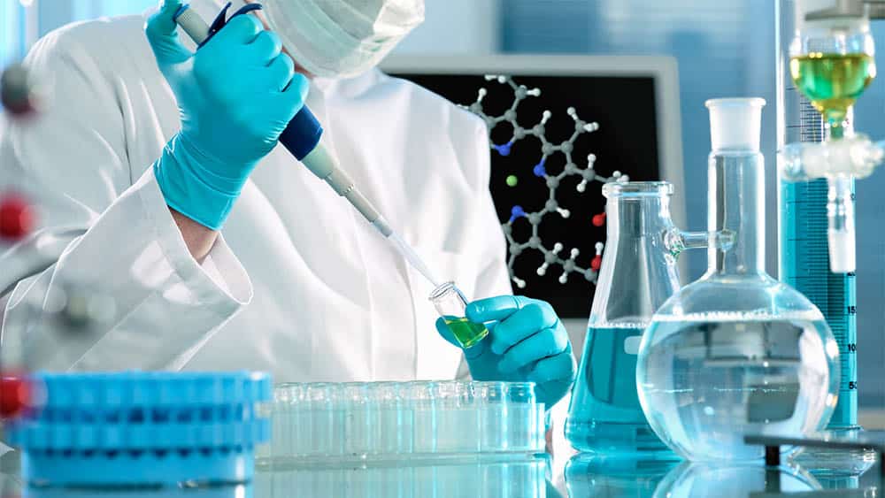 Cientista trabalhando em laboratório com pipeta e frascos.