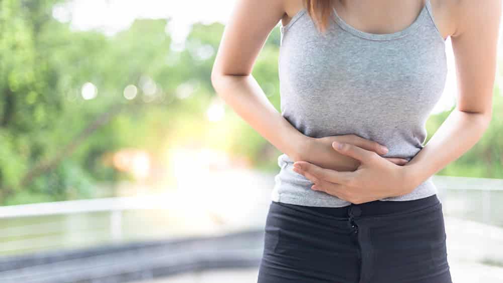Mulher jovem com as mãos no abdômen em sinal de dor, sintoma típico da endometriose.