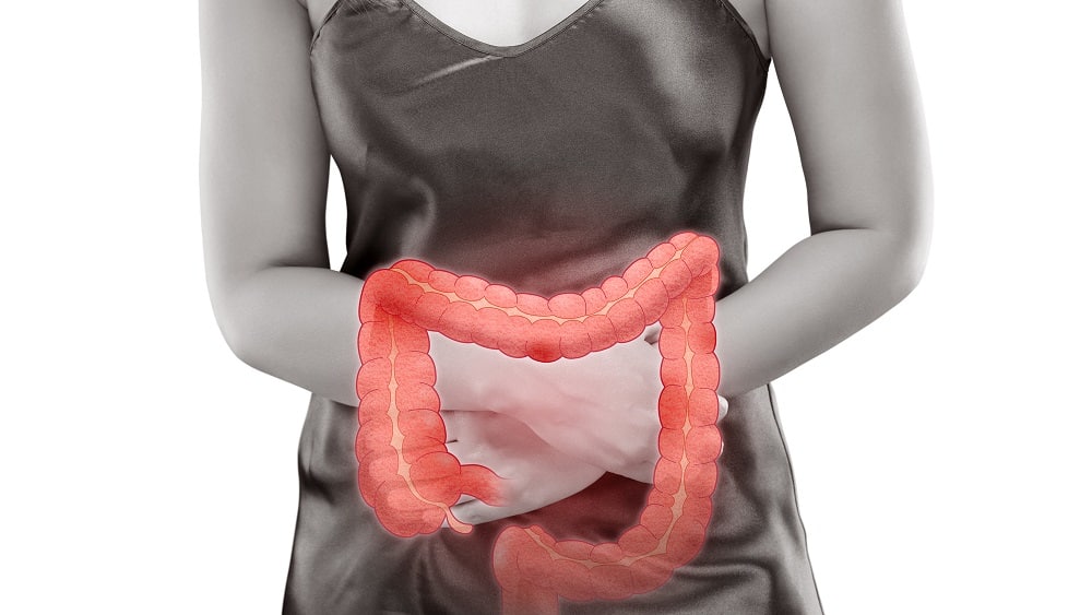 Mulher com as mãos sobre o abdômen, demonstrando a dor causada pela síndrome do intestino irritável