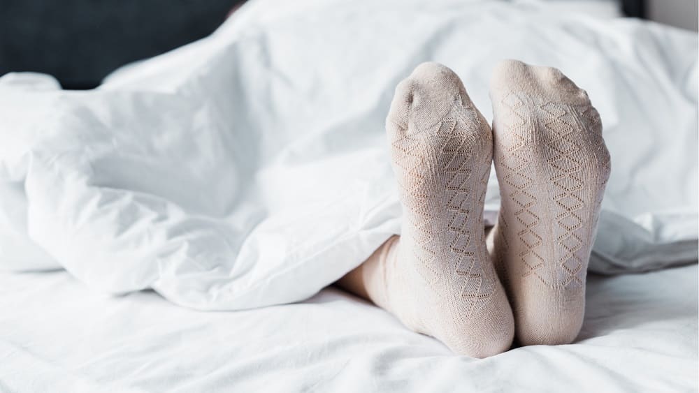 Pessoa deitada numa cama, com somente os pés para fora do lençol