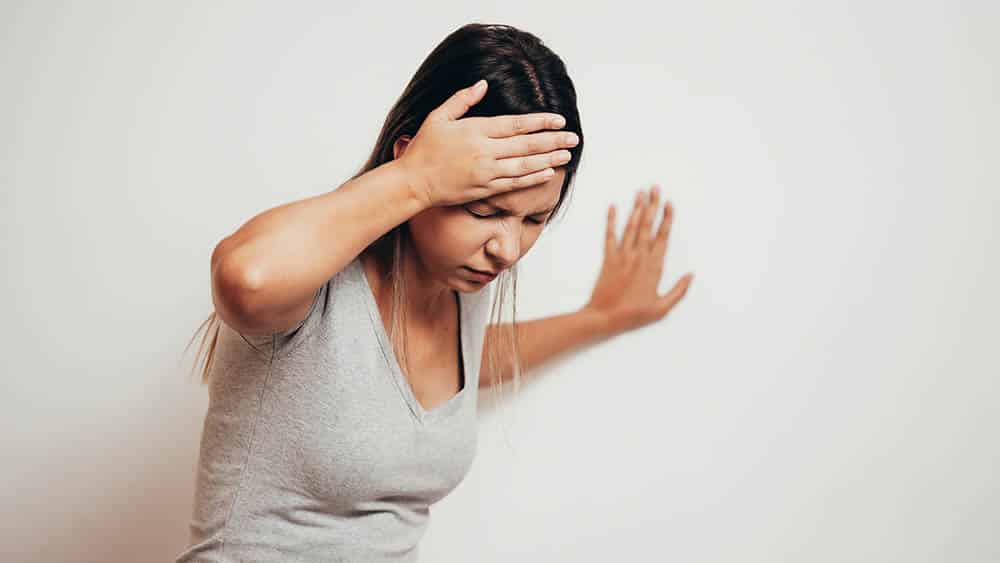 Mulher com mão na cabeça se apoiando em parede indicando tontura, sintoma clássico da labirintite.