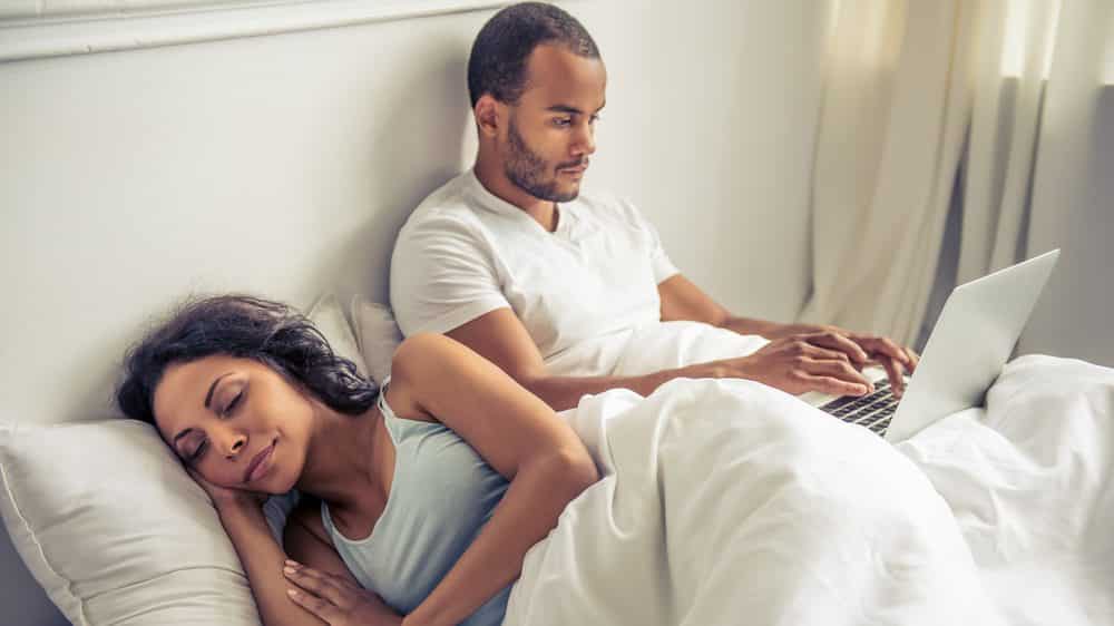 Relógios biológicos mulher dorme na cama ao lado de homem que usa computador e tem relógio biológico diferente