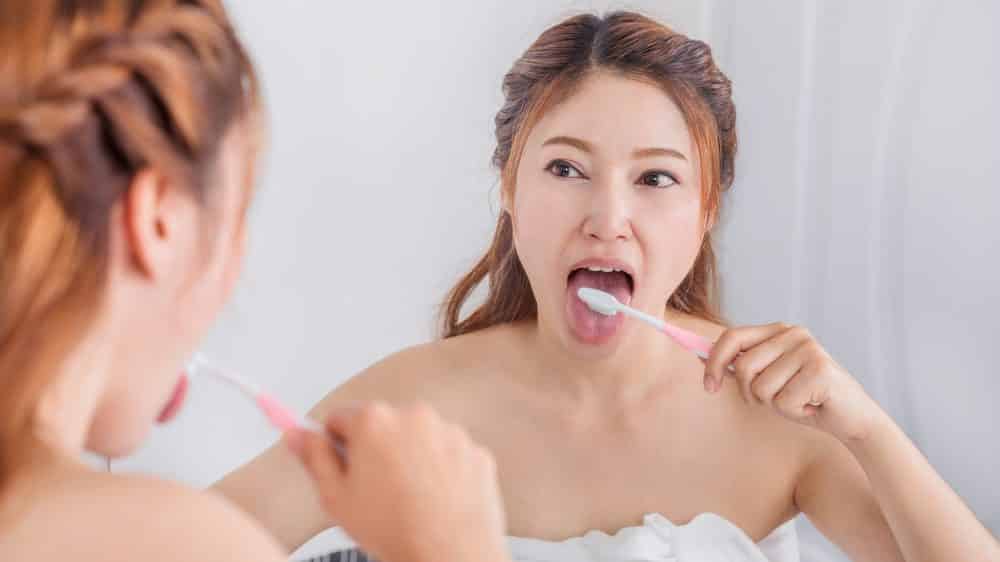 mulher escovando os dentes em frente ao espelho. Combate ao mau hálito inclui higiene bucal