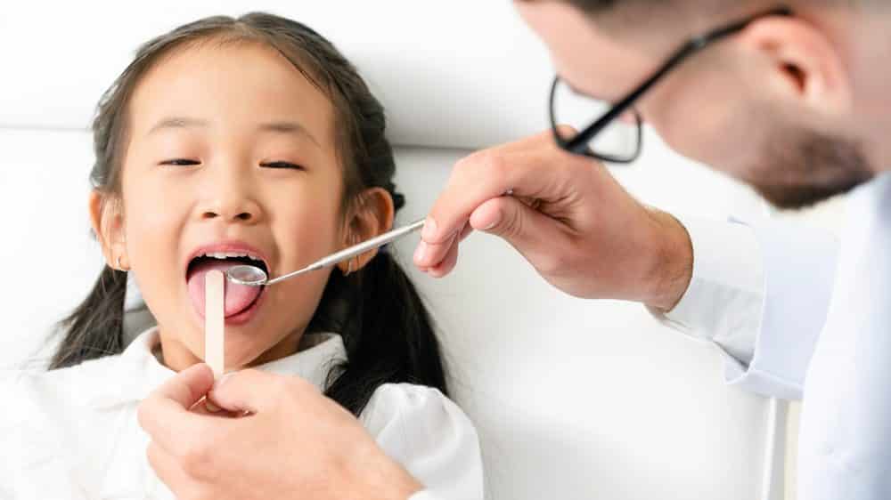 dentista examina boca de menina. Micróbios da boca causam vários problemas bucais