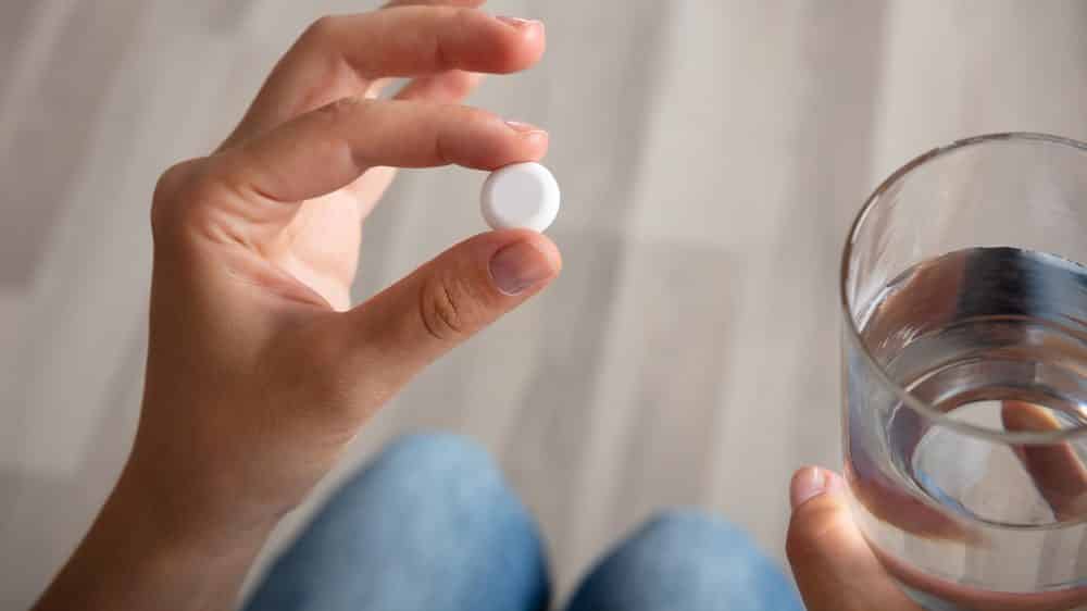 close em mão de mulher segurando comprimido de morfina e copo de água
