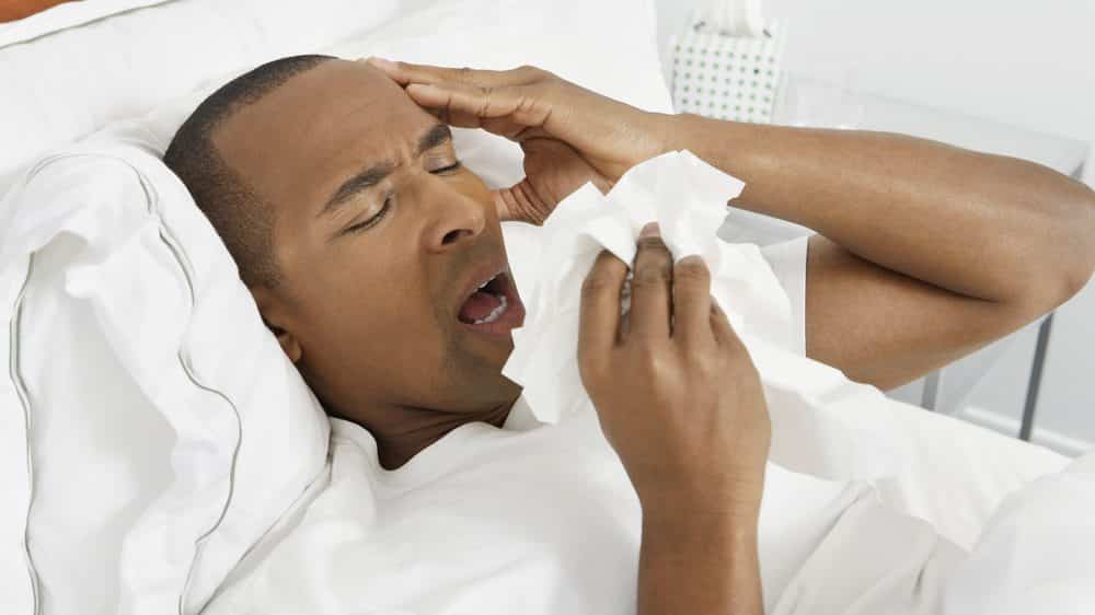 homem doente, de cama, espirrando.veja as condições para a propagação da gripe