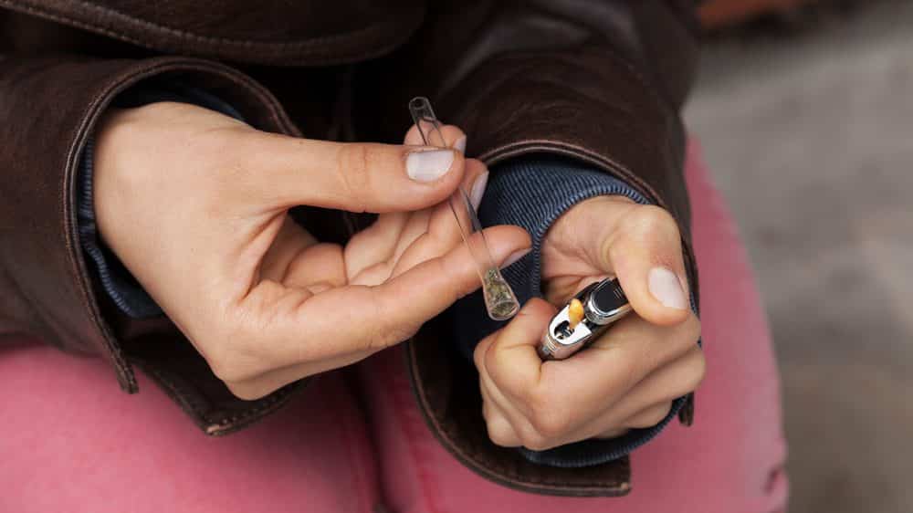 jovem fuma maconha em cachimbo de vidro. droga pode gerar prazer compulsivo