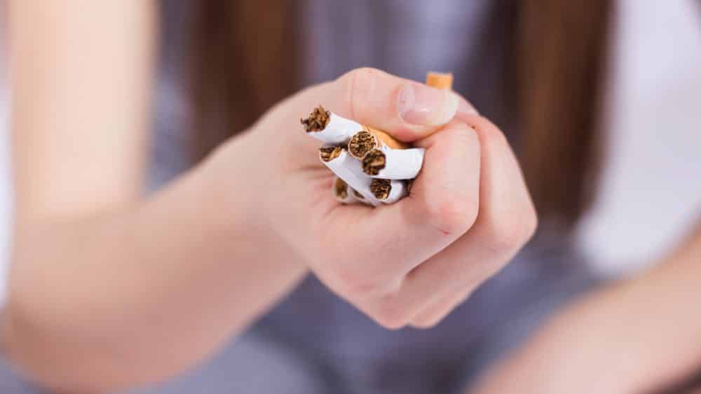 close em mão de mulher amassando cigarros. Parar de fumar envolve cinco fases