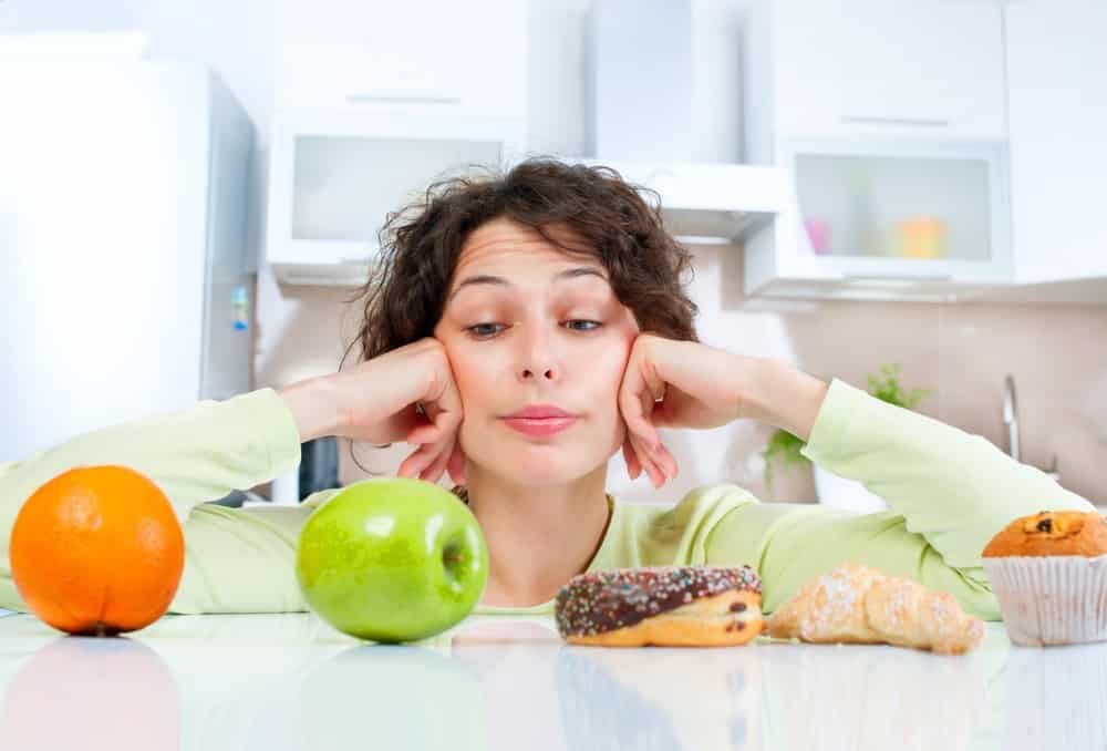 Diabetes e privacidade | Artigo mulher jovem, diante de fruta e doce, fica em dúvida sobre o que comer. Quem tem diabetes deve ingerir pouco açúcar