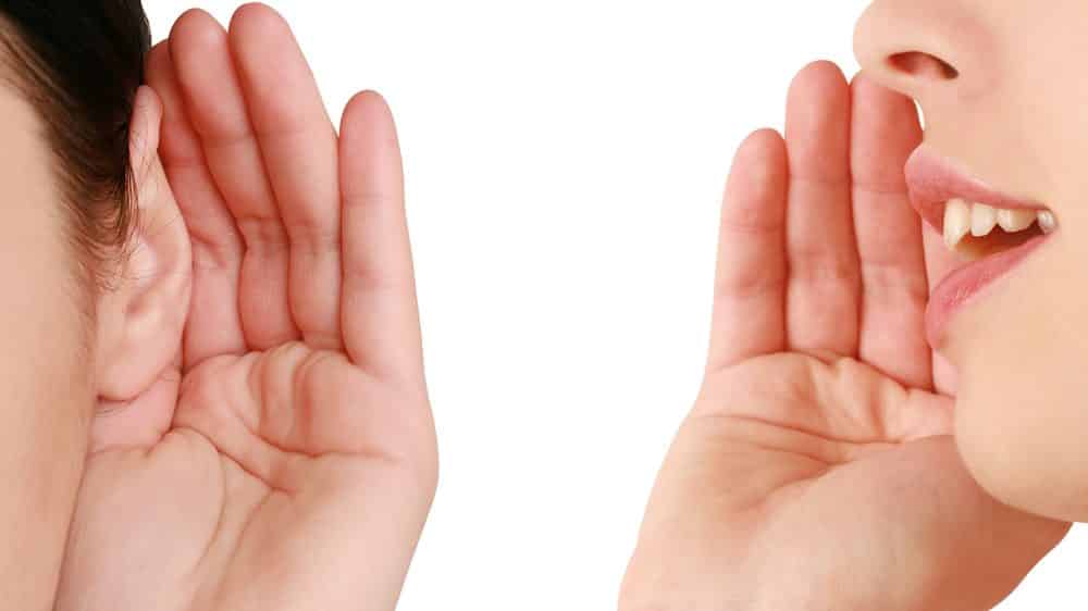 mulher fala, com mão na boca, e outra escuta, com mão na orelha. Evolução da linguagem é tema de debate