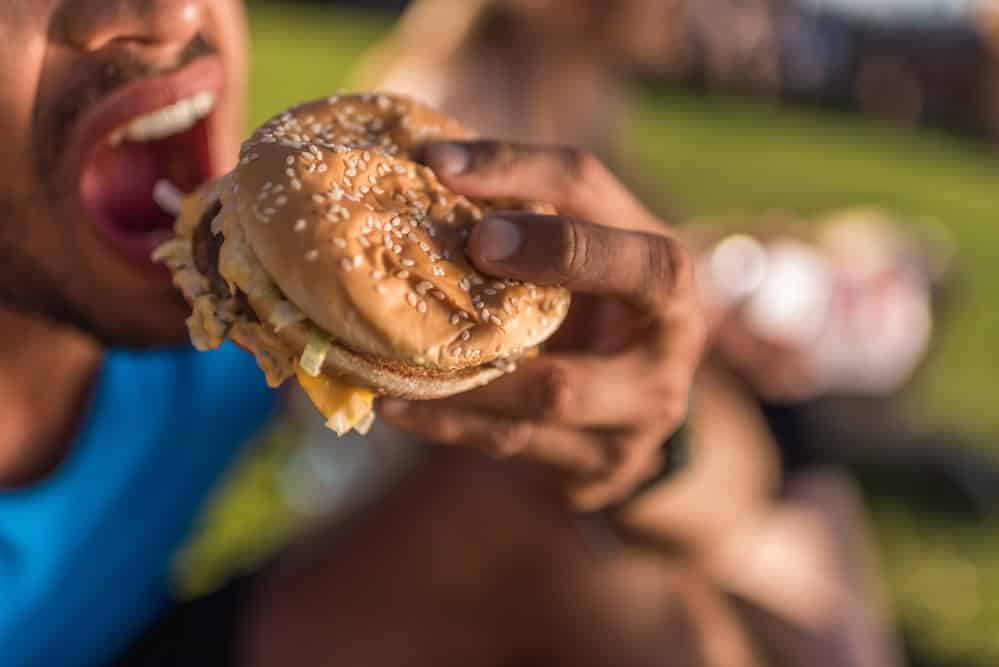 homem dá uma mordida em hambúrguer. Entender os mecanismos envolvidos no controle do apetite pode ajudar a evitar o acúmulo de peso