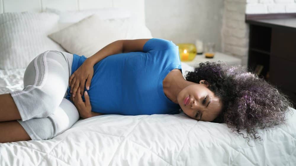 mulher deitada, com mão no abdômen em sinal de cólica menstrual