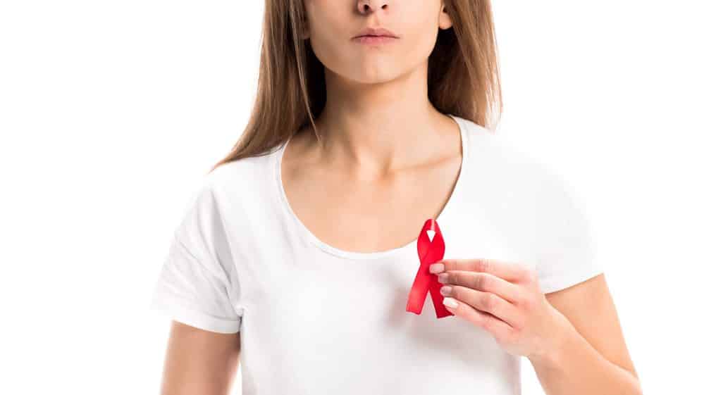 mulher com laço vermelho na camiseta, simbolizando a luta contra o HIV. O sexo feminino sofre preconceito