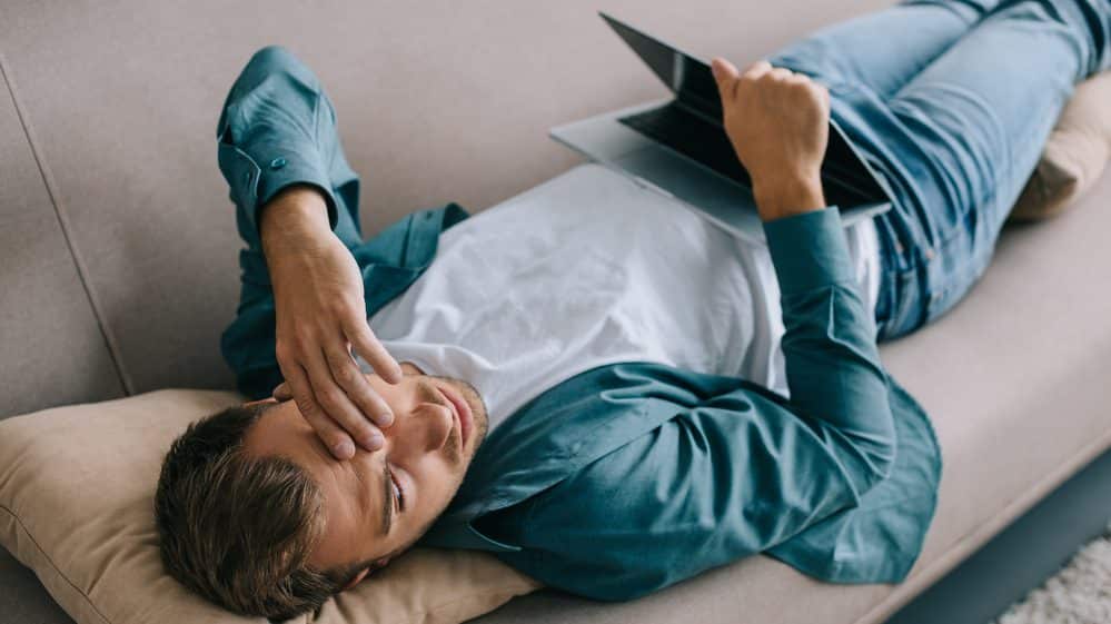 Privação do sono | Artigo homem deitado no sofá, com computador no colo, sonolento