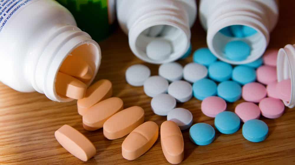 Panaceias modernas | Artigo close em frascos abertos, com comprimidos de vitaminas coloridos caídos sobre uma mesa