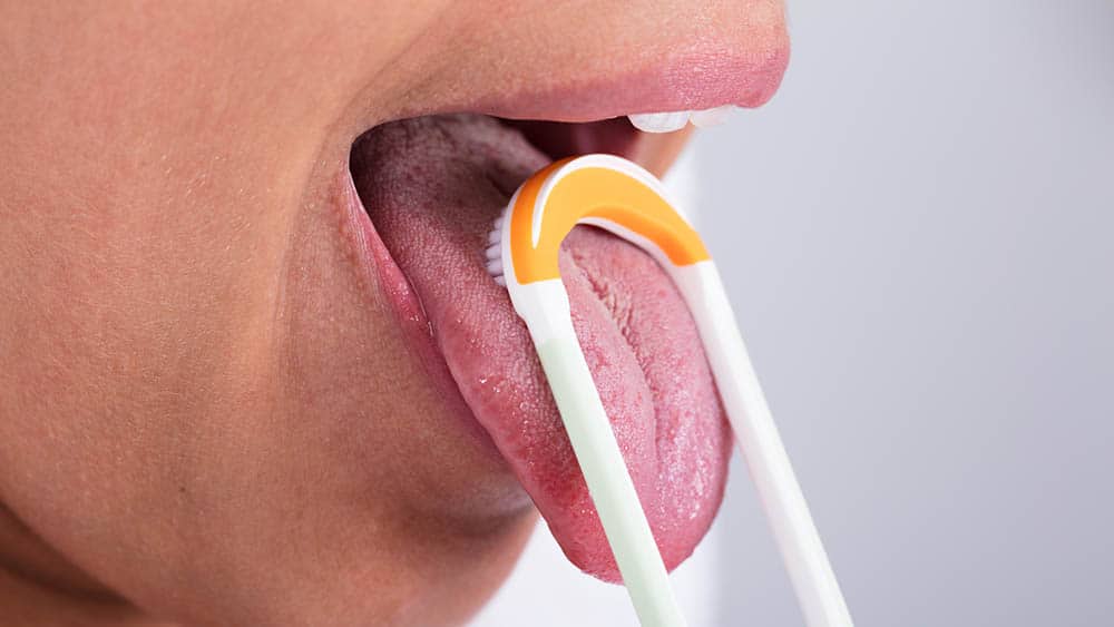 Close em boca de mulher usando raspador de língua.