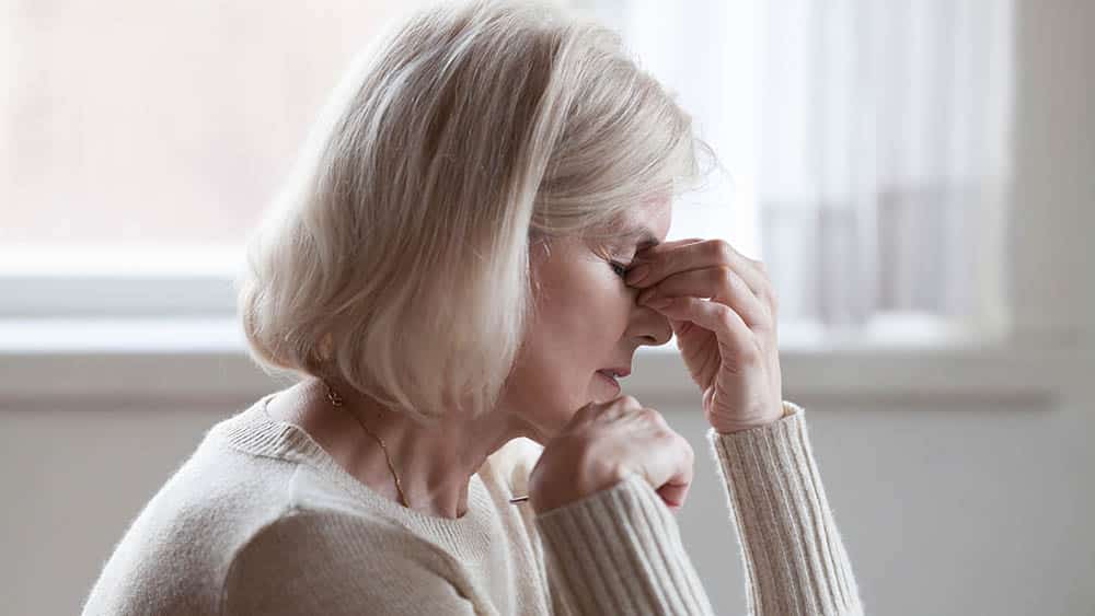 Mulher mais velha de perfil com mão apertando entre os olhos indicando tontura.