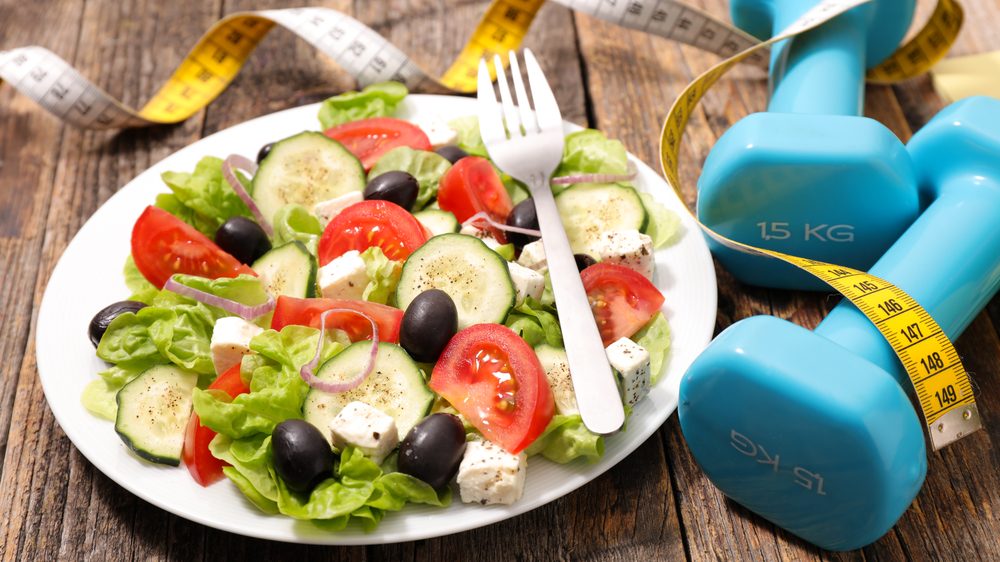 prato de salada, peso e fita métrica sobre a mesa, indicando estilo de vida saudável