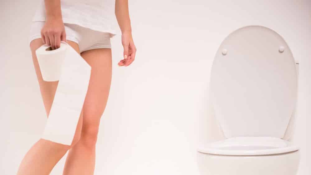 mulher com incontinência urinária segura rolo de papel higiênico em frente ao vaso sanitário.