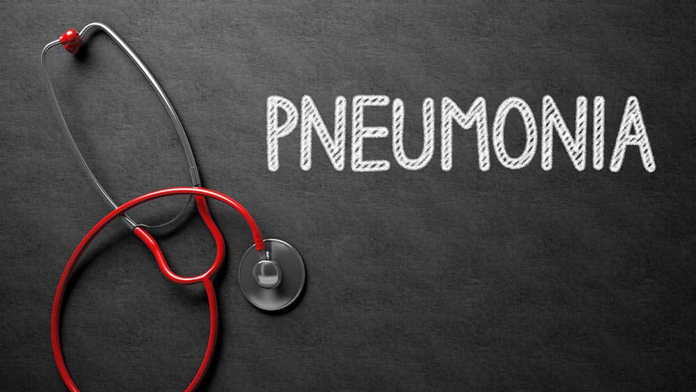 Pneumonia escrito em uma lousa e estetoscópio ao lado.