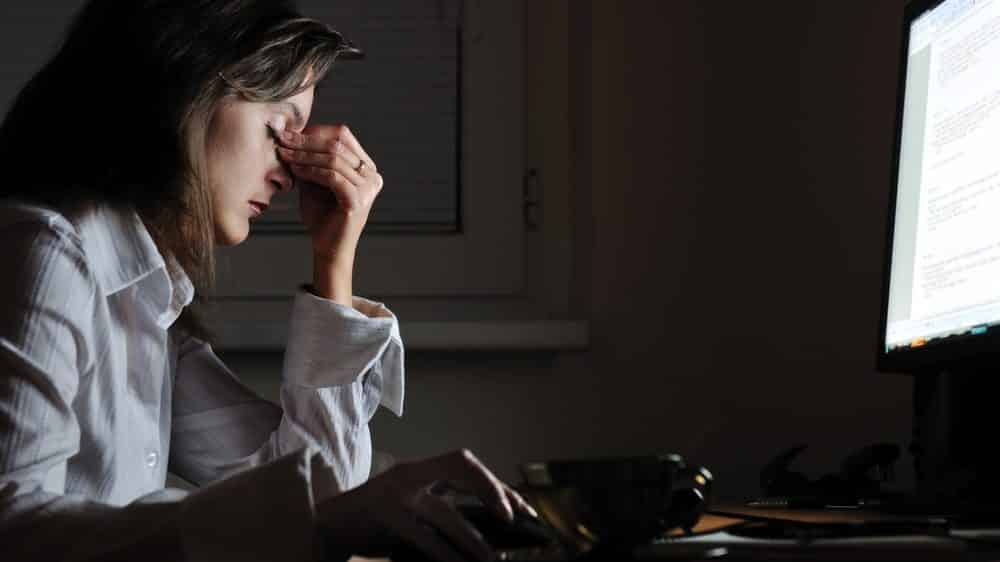 mulher trabalhando diante do computador à noite, com a mão no rosto em sinal de estresse