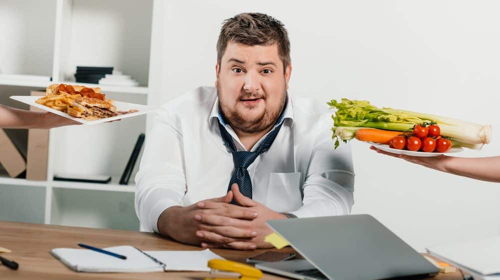 homem gordo sentado enquanto lhe oferecem salada e sanduíche. Dietas para emagrecer não devem ser muito restritivas.