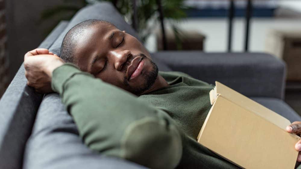 homem dorme no sofá com livro aberto sobre o peito. estudo mostra relação entre falta de sono e diabetes