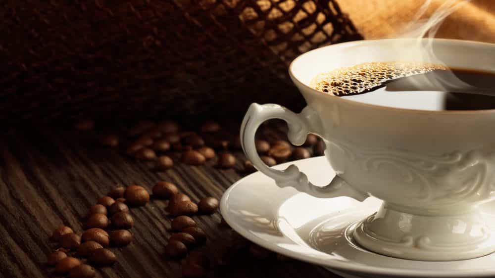 O café e a longevidade | Artigo xícara de café com grãos ao lado. café e diminuição da mortalidade têm relação