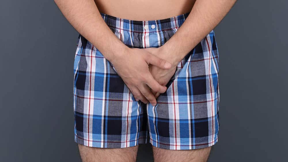 Homem de cueca com as mãos à frente da região do pênis, órgão afetado pela balanite e pela balanopostite.