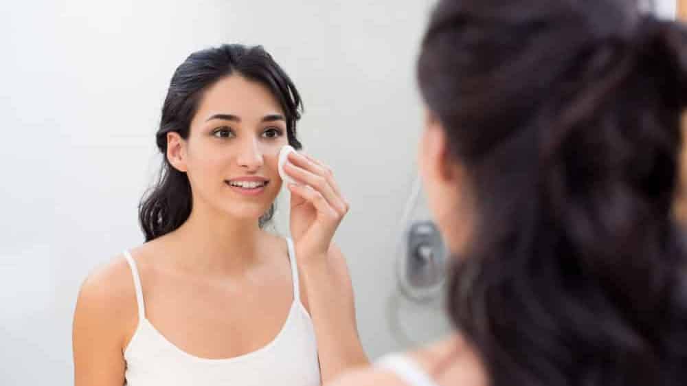 menina limpa o rosto para evitar acnes em frente ao espelho
