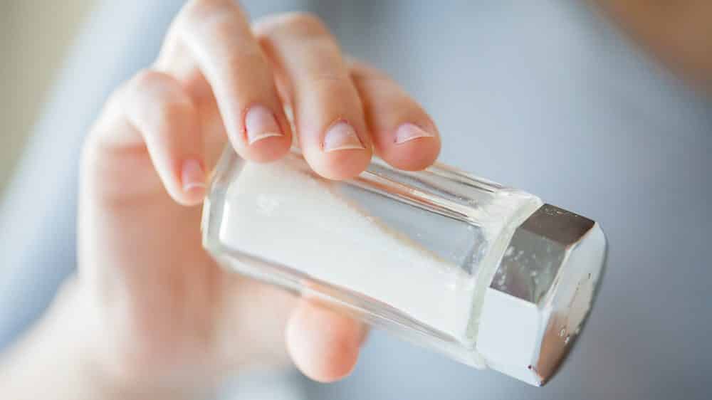 mão de mulher segurando saleiro.excesso de sal faz mal à saúde