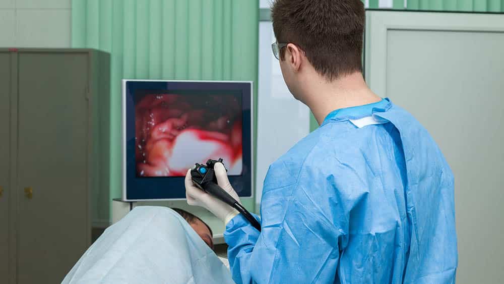 Médico observando monitor e fazendo endoscopia em paciente sedado.