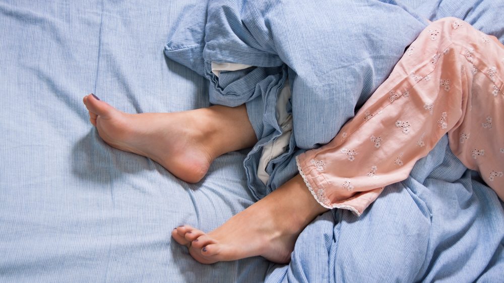 close de pernas de mulher deitada na cama, com síndrome das pernas inquietas