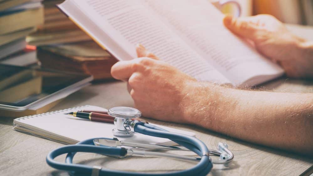 médico estuda em livro, ao lado de estetoscópio.