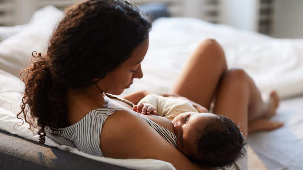 O seio materno | Artigo mulher amamenta filho na cama. veja efeitos protetores da amamentação