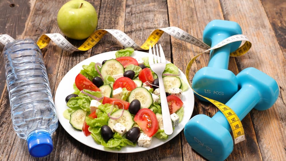 fruta, salada, fita métrica, garrafa de água e pesos sobre a mesa. veja mitos e verdades sobre obesidade