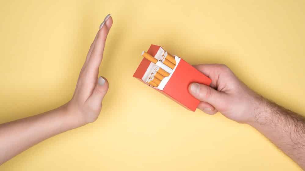 Cigarro: Riscos reais e benefícios de parar | Artigo mão oferece maço de cigarro para outra mão, que recusa para parar de fumar