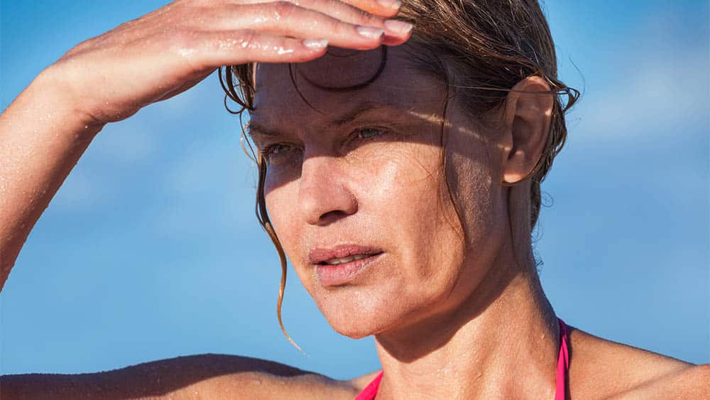 Mulher suada em dia quente protegendo os olhos com a mão.