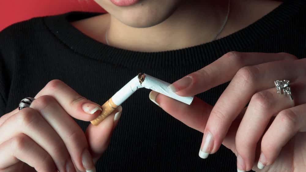 Close de mãos de mulher partindo um cigarro ao meio. mulheres têm mais dificuldade para largar o cigarro.