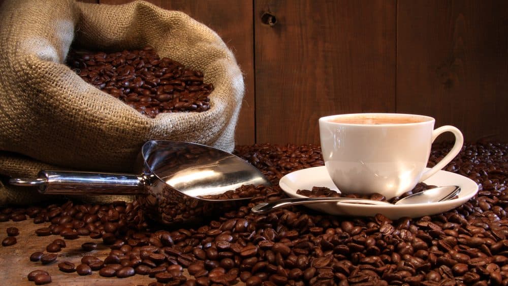 xícara com café em grão e saco de café ao lado. café pode ajudar a reduzir doenças no fígado
