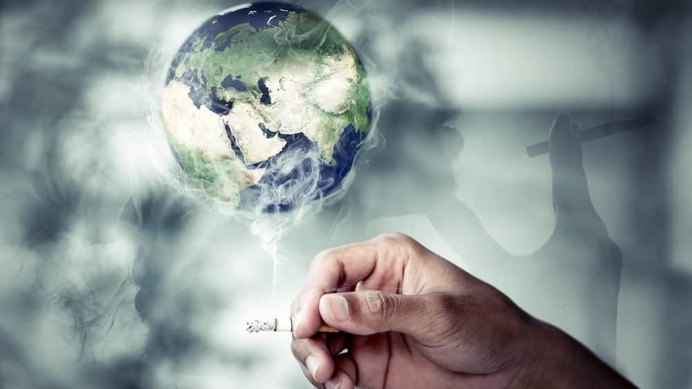 O cigarro no mundo | Artigo mão de homem segurando cigarro com fumaça envolvendo globo terrestre. número de fumantes no mundo ainda é alto
