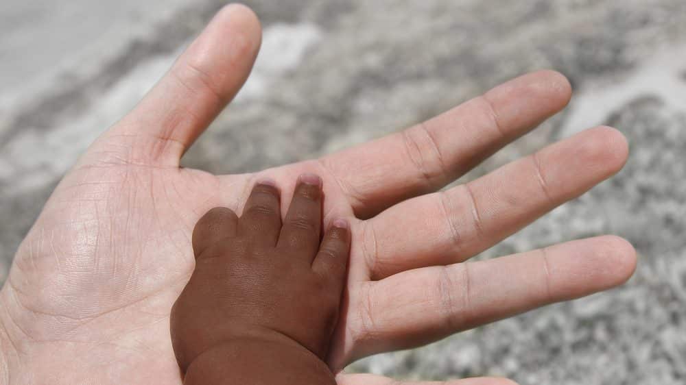mão de bebê negro apoiada em mão de adulto branco. racismo é comportamento evitável