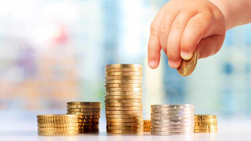 close de mão de bebê amontoando moedas. Pobreza e cognição estão relacionadas