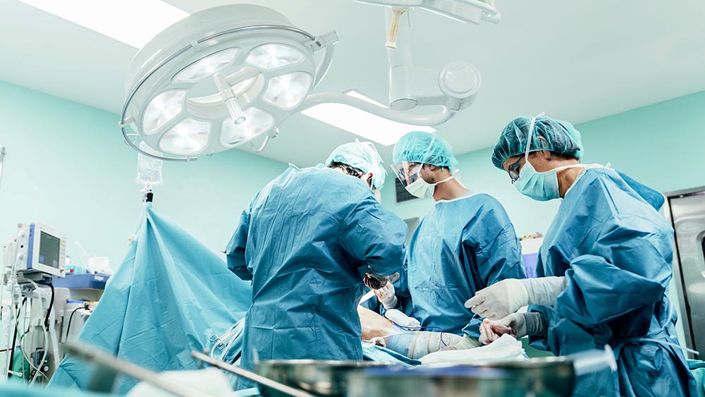 Três médicos operando em uma sala de cirurgia, local mais sujeito a ocorrências de sepse.
